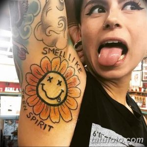 Фото тату: большая татуировка подсолнуха с надписью 'Smell Like Teen Spirit' на руке девушки, выполненная в ярких цветах.