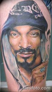Фотография реалистичной татуировки с изображением Snoop Dogg на плече мужчины. Детализированный портрет с банданой и серьгами.