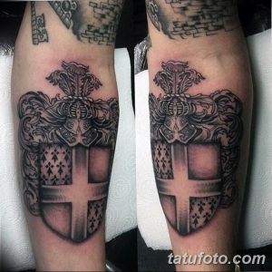Фото гербовой татуировки на предплечье, выполненной в стиле blackwork с использованием плотных черных заливок и четких линий.