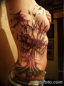 Фото тату дерева жизни на женском боку. Черно-фиолетовая татуировка с летящими птицами, выполненная в реалистичном стиле.