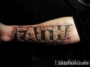Фото тату: татуировка надписи 'FAITH' на предплечье, выполненная в стиле каменной кладки. Черно-серые тона, реалистичная текстура.