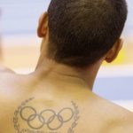 Фото тату: Татуировка на спине, изображающая олимпийские кольца и латинскую фразу 'Citius, Altius, Fortius'. Простой и лаконичный рисунок татуировки.