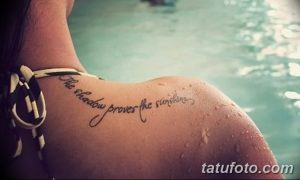Фото тату: черная надпись на плече с цитатой 'The shadow proves the sunshine'. Изящный шрифт и плавные линии.