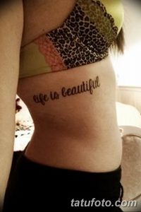Фото тату надписи «life is beautiful» на боку. Черная, изящная каллиграфия, выполненная вдоль линии талии. Простой, но вдохновляющий рисунок татуировки.