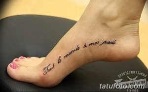 Фото тату: черная надпись на французском языке «Tout le monde à mes pieds» на женской стопе, выполненная изящным шрифтом.