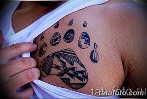 Фото тату стилизованной лапы животного в стиле трайбл на груди. Черно-белый рисунок татуировки с использованием геометрических узоров.