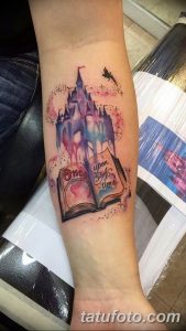 Фото тату на руке: красочный рисунок замка из сказки, открытой книги и летящей птицы, выполненный в акварельном стиле.