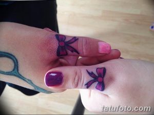 Фото тату: Два маленьких, аккуратных тату бантиков, выполненных в фиолетовом цвете, расположены на лодыжках двух девушек. Изящный дизайн для парных татуировок.