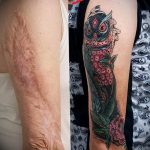 Фото тату совы на руке, покрывающей шрамы от ожогов. Цветная татуировка с детальной проработкой перьев и яркими цветами.