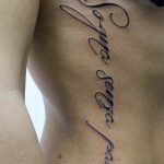 Фото татуировки с надписью на боку. Текст выполнен красивым каллиграфическим шрифтом в черном цвете.