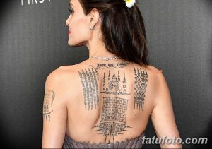 Фотография Анджелины Джоли с татуировками на спине и плече, включая надписи на кхмерском языке и геометрические узоры. Детализированное изображение татуировок.