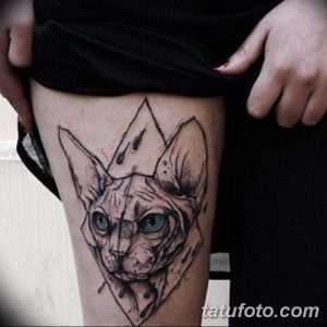 Фотография реалистичной татуировки кота породы сфинкс с яркими голубыми глазами на бедре. Детализированный рисунок с использованием теней и линий.