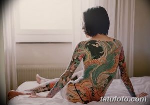 Фото тату на спине и руках женщины, выполненное в японском стиле с изображением карпа кои, цветов и волн. Яркие цвета и детализированная проработка.