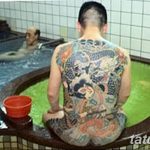 Фото тату японского дракона на спине мужчины, расслабляющегося в горячем источнике онсене. Детализированный рисунок татуировки в традиционном стиле.
