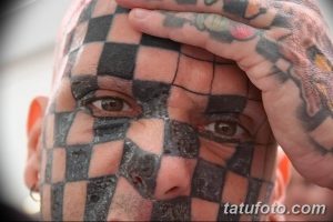 Фото тату: крупный план лица Мэтта Гона, "Человека-шахматной доски", с татуировкой в виде черно-белой шахматной сетки, частично закрытой рукой.