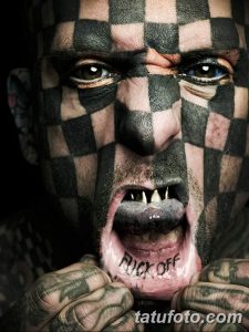 Крупный план лица мужчины с клетчатой татуировкой и надписью 'FUCK OFF' на губе. Выражение лица агрессивное.