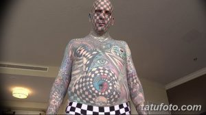 Фотография мужчины с полным татуированным телом, включая лицо, покрытое черно-белой клеткой. Видна татуировка на животе.