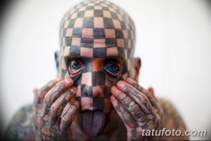 Фото тату: лицо и руки полностью покрыты черно-белой шахматной татуировкой. Мужчина высунул язык, демонстрируя татуировку на нем.