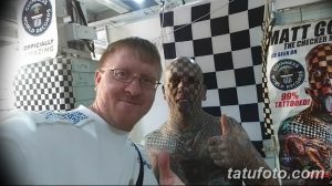 Фото тату: мужчина с почти полностью покрытым татуировками телом позирует с фанатом на фоне баннера с надписью "Guinness World Records".