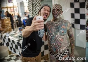 Фотография мужчины с татуировкой в виде шахматной доски на лице, позирующего с другом. Оба мужчины выглядят экспрессивно и радостно.