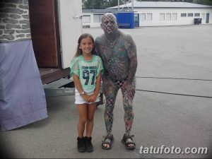 Фото тату: мужчина с шахматной татуировкой на теле стоит рядом с маленькой девочкой. Татуировка покрывает все тело мужчины.