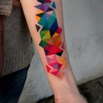Фото тату: красочный рисунок геометрических фигур, треугольников, расположенных вдоль предплечья. Современный стиль, яркие цвета.