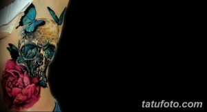 Фото татуировки на боку, изображающей череп, украшенный бабочками и розой. Цвета: черный, розовый, голубой.