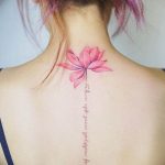 Фото тату лотоса на спине, с ниспадающей надписью. Изящный рисунок татуировки выполнен в розовых тонах.