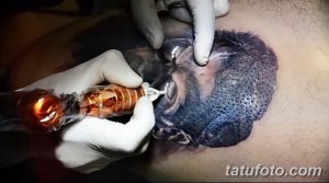 Фотография процесса нанесения реалистичной татуировки портрета на спину. Видна тату-машинка и детализированное изображение.