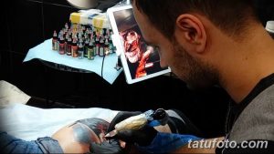 Фотография процесса нанесения татуировки на тело. Мастер использует планшет с изображением референса.