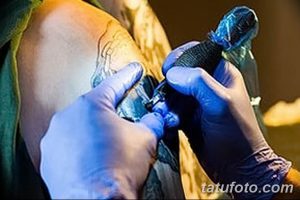 Фото тату: мастер тату наносит рисунок на кожу клиента, используя тату-машинку. Видны рука мастера и участок кожи.