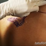 Фотография процесса переноса эскиза татуировки бабочки на лопатку девушки. Мастер использует трафарет и маркер.