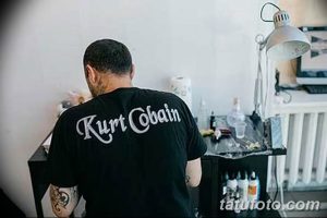 Фото татуировки на спине: надпись "Kurt Cobain" выполнена стилизованным шрифтом, черным цветом.