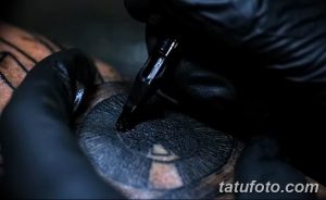 Крупный план процесса нанесения татуировки. Видна тату-машинка, рука мастера в перчатке и кожа клиента с начинающимся рисунком.