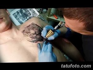 Фото процесса нанесения татуировки тигра на груди мужчины. Мастер тату работает над деталями морды тигра, используя тату-машинку.