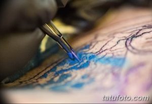 Фото крупным планом процесса нанесения цветной татуировки с использованием синих и фиолетовых чернил. Видна игла тату-машинки.