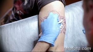 Фото тату эскиза на плече, мастер наносит контур рисунка. Видны линии эскиза и рука в голубой перчатке, контролирующая процесс.