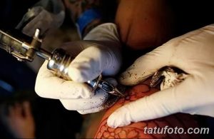 Фотография процесса нанесения татуировки: рука мастера в белых перчатках работает тату-машинкой над кожей, на которой уже виден рисунок.