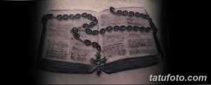 Фото тату на спине, изображающее открытую книгу с крестом и четками. Детализированная черно-серая татуировка с религиозным сюжетом.