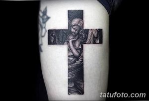 Фото тату на плече, изображающее крест, в центре которого находится ангел. Детализированная черно-серая татуировка с религиозным сюжетом.