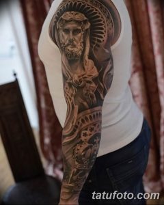 Фото тату на руке с изображением Иисуса Христа. Детализированный рисунок в черно-серых тонах, с акцентом на лицо и одежду.