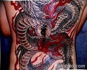 Фото тату огромного дракона, покрывающего спину. Детализированный рисунок татуировки с использованием красных, серых и черных оттенков.