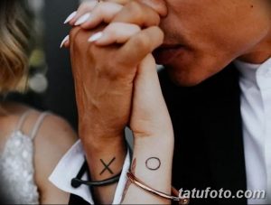 Фотография рук пары, держащихся за руки, с татуировками 'X' и 'O' на запястьях. Символизирует любовь и привязанность.