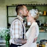 Фотография пары, обнимающейся в интерьере с татуировками на руках. Жених целует невесту.
