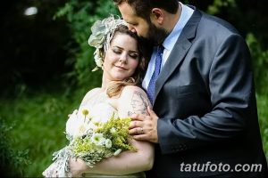 Фото пары на свадьбе. У невесты на плече видна татуировка с изображением женского профиля. Невеста держит букет.