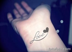 Фото тату надписи 'Love' и сердца на запястье, выполненное в черном цвете. Изящный шрифт и аккуратные линии.