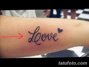 Фото тату надписи 'Love' на женском запястье, выполненной черными чернилами. Небольшое изображение сердца дополняет композицию.