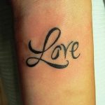 Фото тату надписи 'Love', выполненной изящным шрифтом на запястье. Минималистичный и стильный рисунок татуировки.