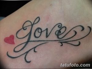 Фото тату на коже: надпись 'Love' выполненная красивым каллиграфическим шрифтом, с маленьким красным сердечком.