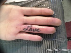 Фотография минималистичной татуировки со словом 'Love' на пальце руки. Черный рисунок татуировки выполнен тонкой линией.